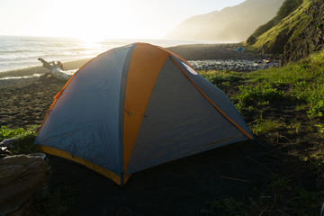 Backpacking tent sits on the black sand of the Lost Coast backpacking trail in California at sunset