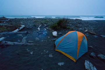 Backpacking tent sits on the black sand of the Lost Coast backpacking trail in California at sunset