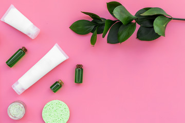 Natural cosmetics for skin care near green leaves on pink background top view copy space