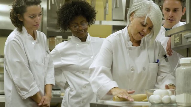 Chef teaching catering students how to roll pastry.