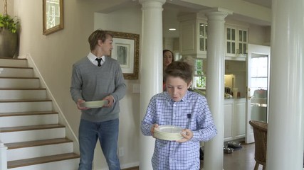 Boys helping mother and grandmother to lay dinner table.