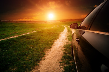 car on a dirt road in a field of sunflowers and wheat with sunlight