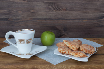 A cup of tea, homemade cookies and an apple on a background of wooden boards.