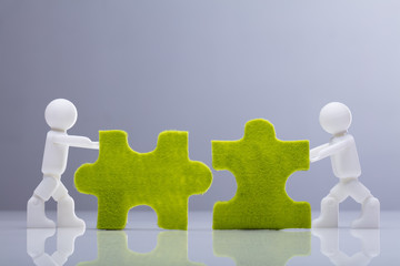 Two Miniature Human Figures Solving Green Jigsaw Puzzles
