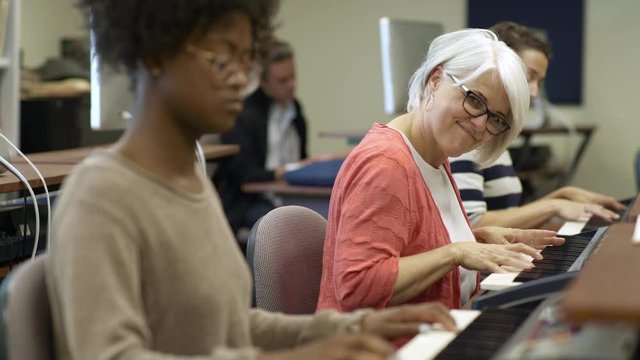 Women playing electric keyboards in college music lesson and smiling towards camera.