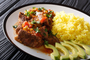 Ecuadorian seco de chivo goat meat with a garnish of yellow rice and avocado close-up. horizontal