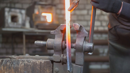 Close up view - hands of Blacksmith with gloves in forge makes steel knife