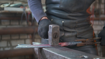 Muscular man blacksmith with hammer in forge creating steel knife