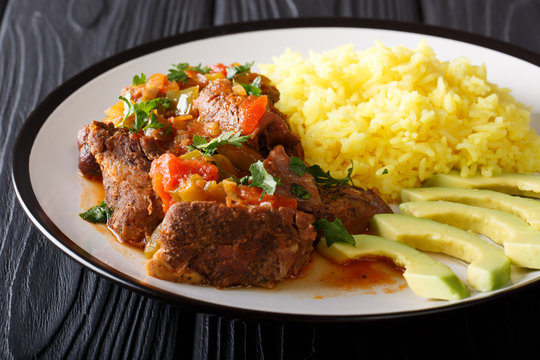 Ecuadorian seco de chive stewed goat meat with a side dish of yellow rice and avocado close-up on a plate. horizontal