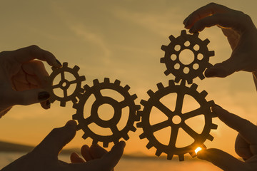 gears in the hands of a team of people against the backdrop of the setting sun, work in a team.