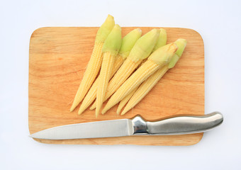 Baby corn and knife on cutting board isolated on a white background. Top view.