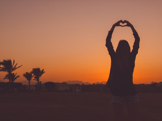 Girl holding heart shape in the sunset / sunrise time.