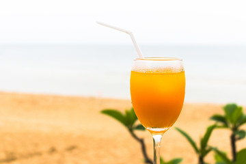 Glass of orange juice with backdrop green leaves and sand beach and sea background.