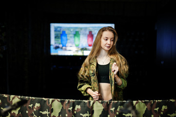 Military girl in camouflage uniform against army background on shooting range.