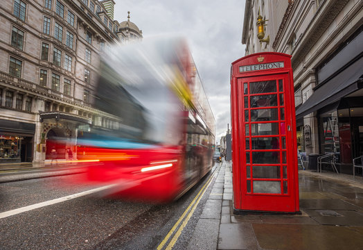 London, England - Iconic blurred red double-decker bus on the move with traditional red telephone box in the center of London at daytime