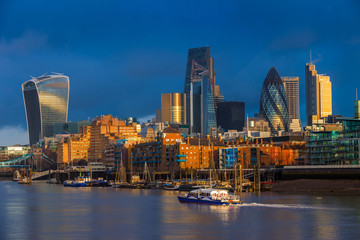 London, England - Skyscrapers of Bank, the leading financial district of London at golden hour with sightseeing boat and colorful dark sky and clouds