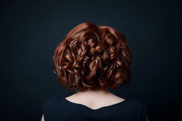 Hair bob with short curls on the female head with red hair rear view against the background of black isolate.