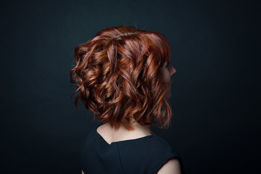 Hair Bob With Short Curls On The Female Head With Red Hair Side View Against The Background Of Black Isolate.