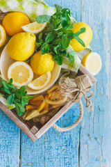 Yellow lemons with mint leaves, wooden background