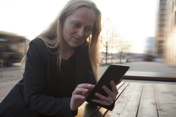 Mujer de negocios sentada en una terraza de la calle lee y escribe en su tablet.