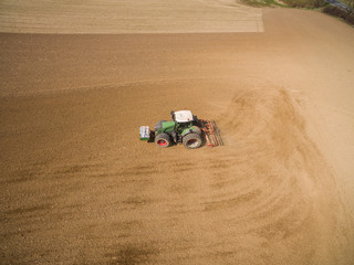 Obraz premium aerial view - tractor plows a agricultural field in spring and prepares it for sowing