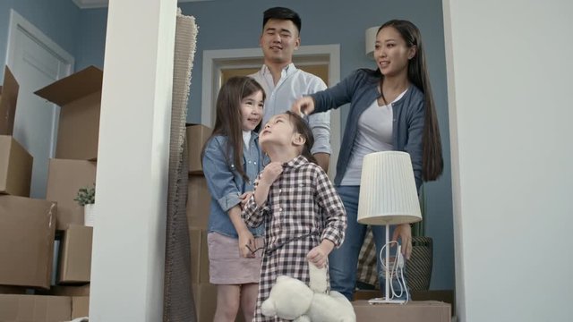 PAN of happy Asian family with children looking around their new house after moving