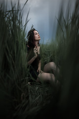 Pretty woman sitting on the grass in dark dress. Beautiful woman posing in tall grass. Brunette lady in field at sunset. Freedom concept background - 201461813