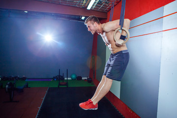 Muscle-up exercise young man doing intense cross fit workout at the gym on gymnastic rings.