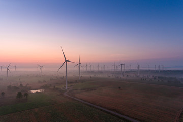 Aerial view of wind turbine sunrise in forested with fog . Sustainable development, environment friendly, renewable energy concept.