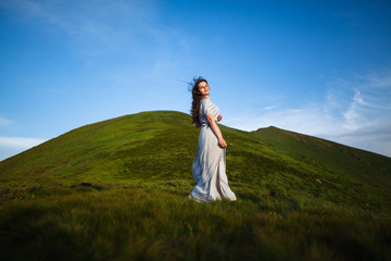 Beautiful woman in dress running in the mountains. Beautiful girl looking happy and smiling. Relaxing, feeling alive, breathing fresh air, got freedom from work. Flowers in the mountains