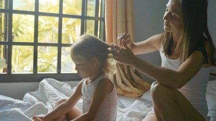 Obraz premium Young mother sits on the bed and combing her daughter.