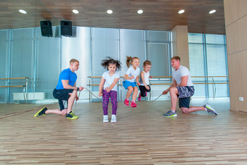 Smiling cheerful kids in school age playing together with jumping rope in gym. Children at physical education lesson in school gym.