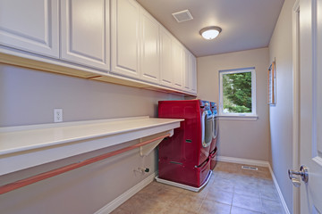Narrow home laundry with white cabinets and red appliances.
