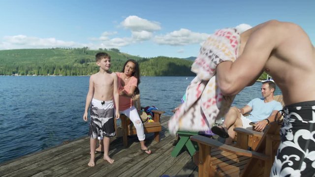 Mother applying sun cream to son by lakeside, family sunbathing in background, Lake Connaught, Washington, USA.