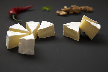Slices of cheese camembert or brie  with walnuts and chili pepper. Milk production. Side view.