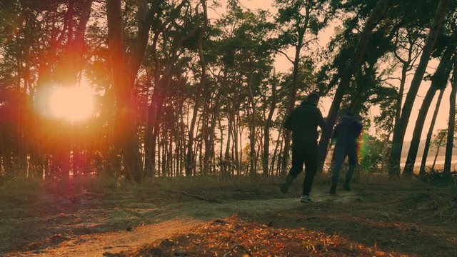 Two athletes running around in the woods. Group of people engaged in sports. Beautiful forest, sun rays through trees, golden sunset. The concept of sport and healthy lifestyle. Slow motion.
