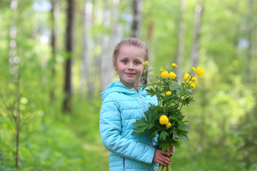 Adorable funny child, blonde healthy toddler girl enjoying nature, playing, hiking and hiding behind the tree in spring or summer forest with flowers