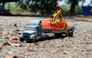 Toy backhoe car on the toy Big truck on gravel floor. They are toys for children.