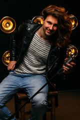 man with long hair sitting on a chair in his hands with a microphone, smilling