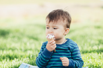 Fototapeta premium Cheerful child in a blue sweater eating ice cream on a background of grass, outdoors