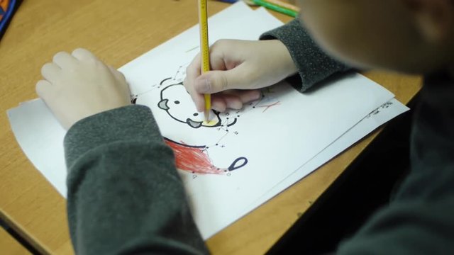 High angle view of boy drawing with color pencil on paper at desk in classroom. Clip. A cute little boy drawing with a pencil close up