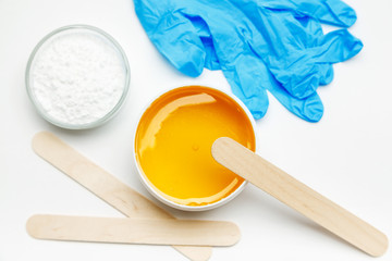 Wax for depilation with blue gloves and other tools on a white background, top view