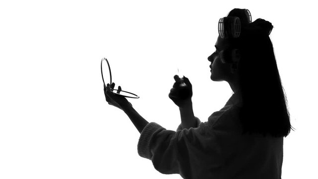 Young woman looking in mirror and applying makeup, preparing for date, beauty