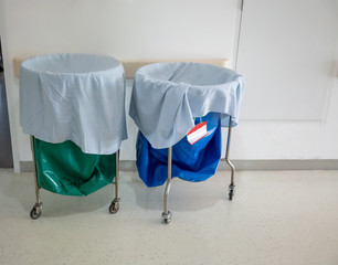 A pile of used clothes and infectious substances in hospital movable trolley with green bag and blue bag.