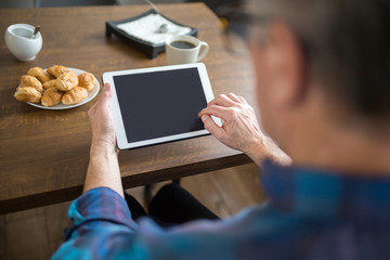 Senior man holding tablet at kitchen table