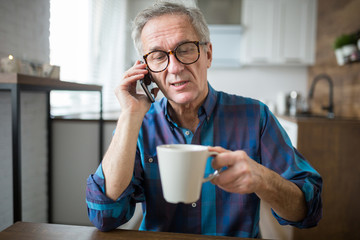 Senior man talking on mobile in kitchen