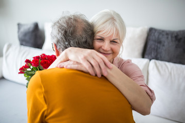 Senior lady hugging her husband holding bunch of roses