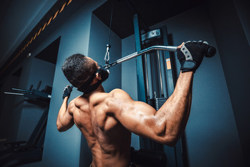 african american athletic man doing exercise in pull down machine back view. black fitness man...