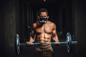 Fototapeta na wymiar african american athletic man in mask looking at camera and lifting barbell on biceps. Exercise for biceps with barbell. black man in gym