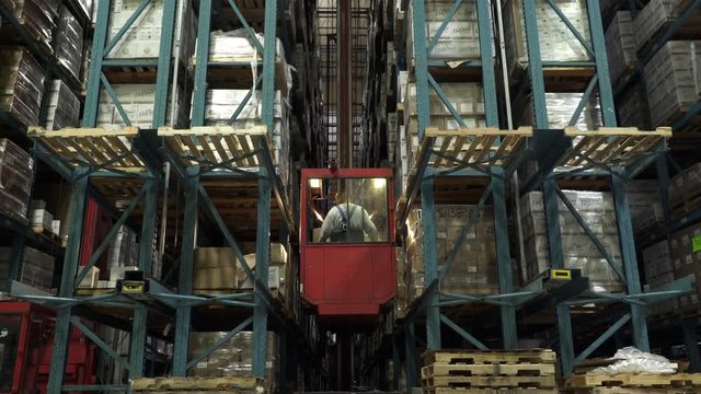 Man operating forklift, reversing, lifting and placing pallet on shelving in warehouse.